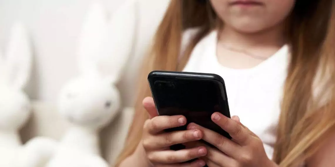 Young-child-holding-smartphone-alone-illustrating-the-importance-of-parental-awareness-of-summer-screen-time.jpg