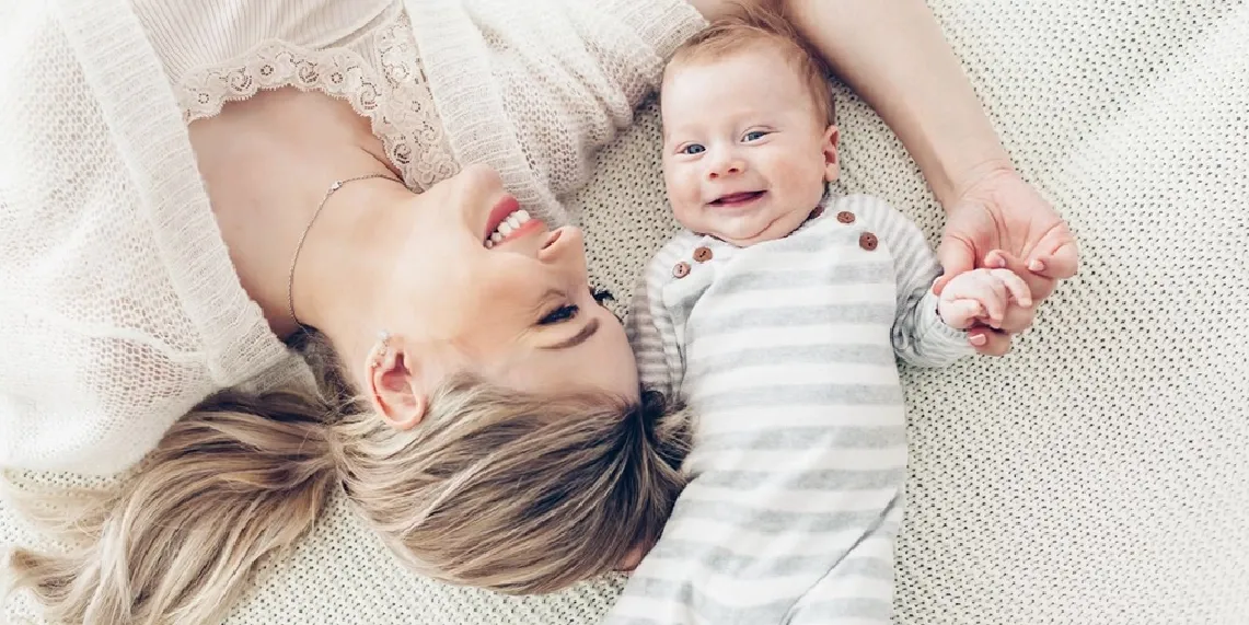 Mom and baby lying together smiling showing joy and connection during postpartum recovery